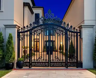 Ornate wrought-iron driveway gate lit at dusk