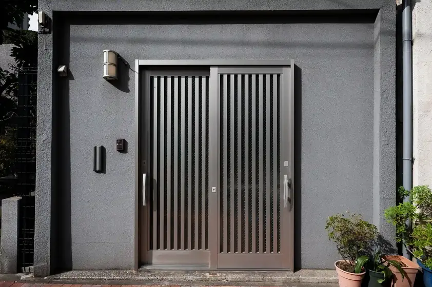 Modern slatted metal sliding door on a grey facade