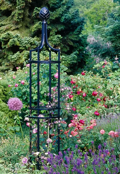 Iron obelisk trellis among flowering garden beds