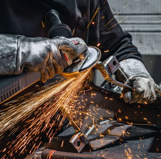 Metalworker in leather gloves grinding steel as sparks fly