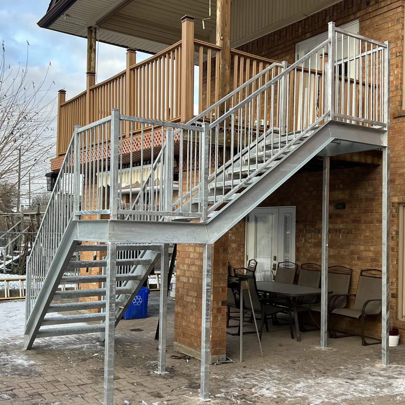 Galvanized steel exterior staircase and railings behind a brick house in winter